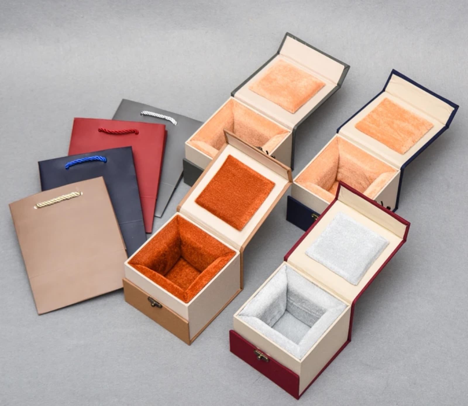 Open rigid gift boxes with fitted fabric-lined interiors and matching paper bags